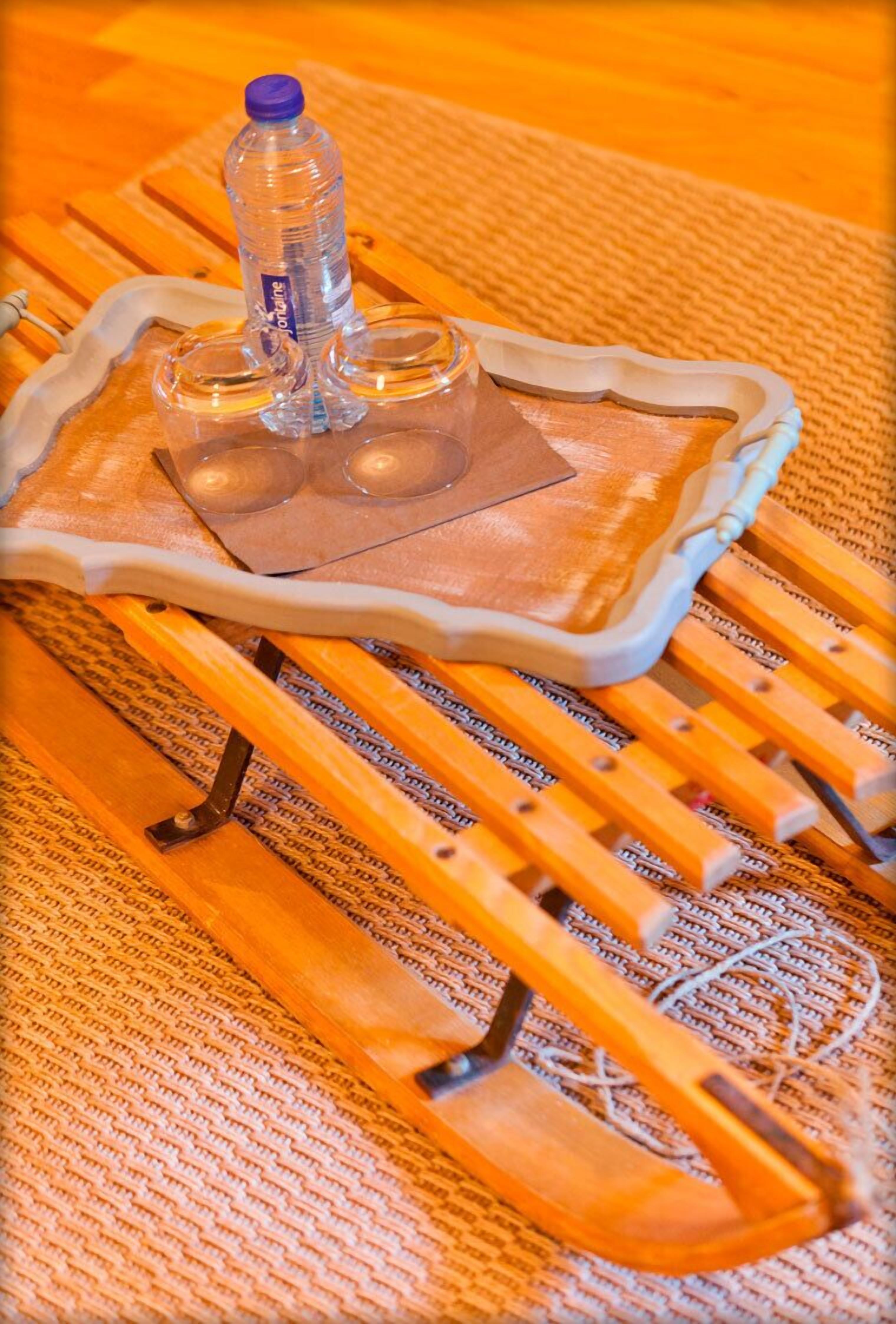 A wooden sled with a plastic bottle and two clear glasses on it.