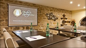 A conference room with a stone wall, a projector screen displaying a logo, and a table set with water bottles and glasses. - Clos de la Gourmandière (Saint-Lothain)