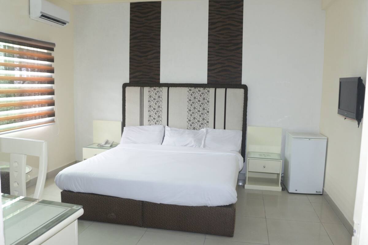 Een hotelkamer met een groot bed, nachtkastjes, een televisie en een raam met zonwering.