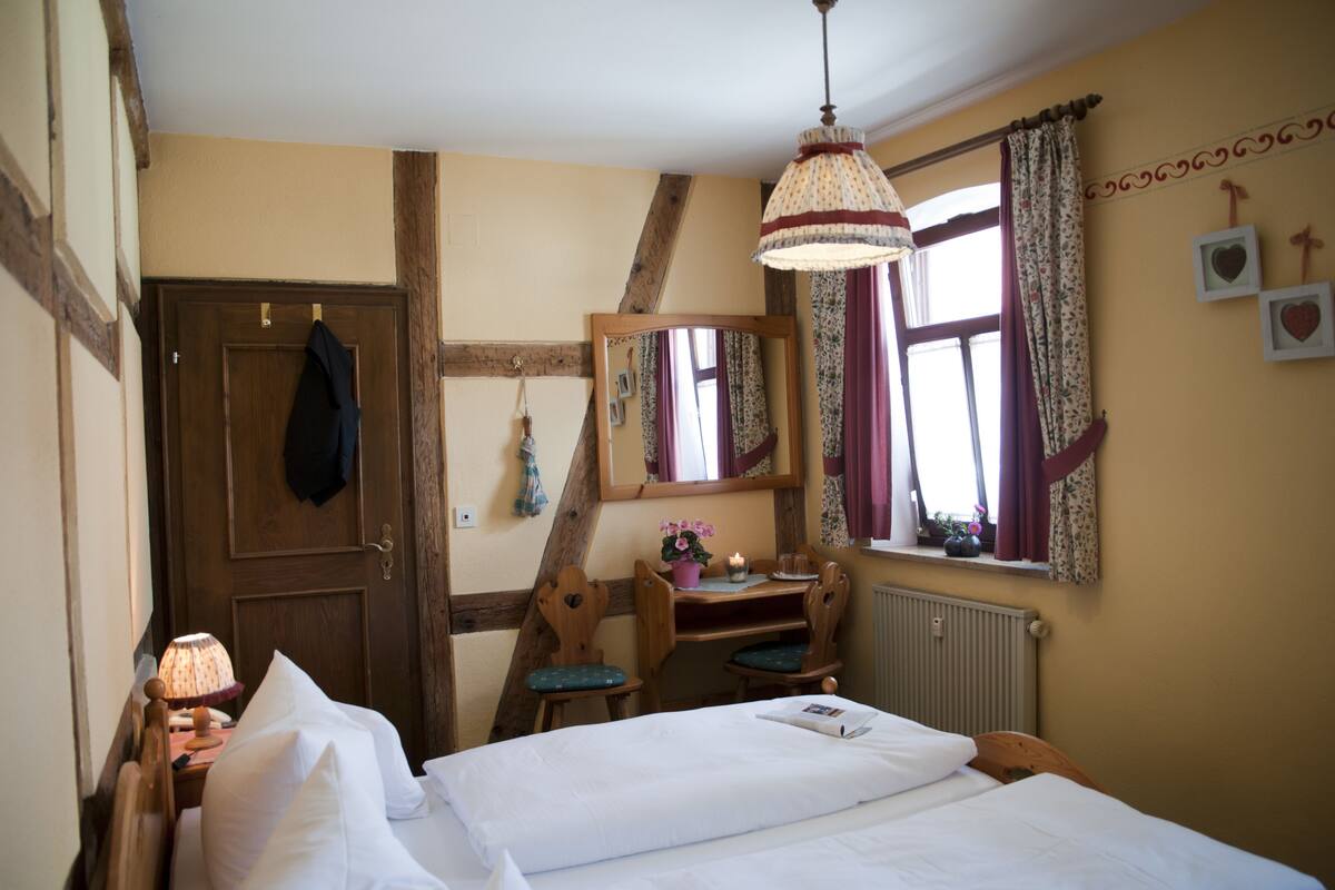 A bedroom with a bed, a desk, a chair, a mirror, and a window with curtains.