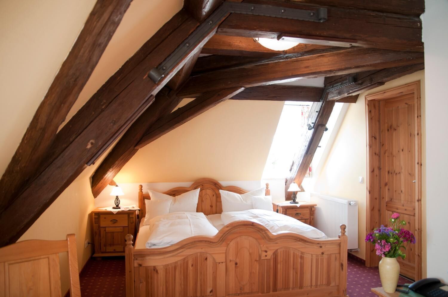A bedroom with a wooden bed, a nightstand, a lamp, a radiator, and a wooden door.