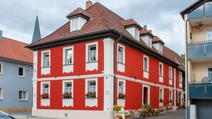A red and white building with multiple windows, a tiled roof, and a small outdoor seating area with tables and chairs.