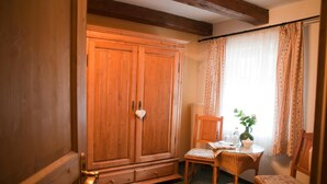 A room with a wooden wardrobe, a small table with chairs, and a window with curtains.