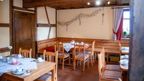 A dining area with wooden tables and benches, white tablecloths, and a rustic ceiling.
