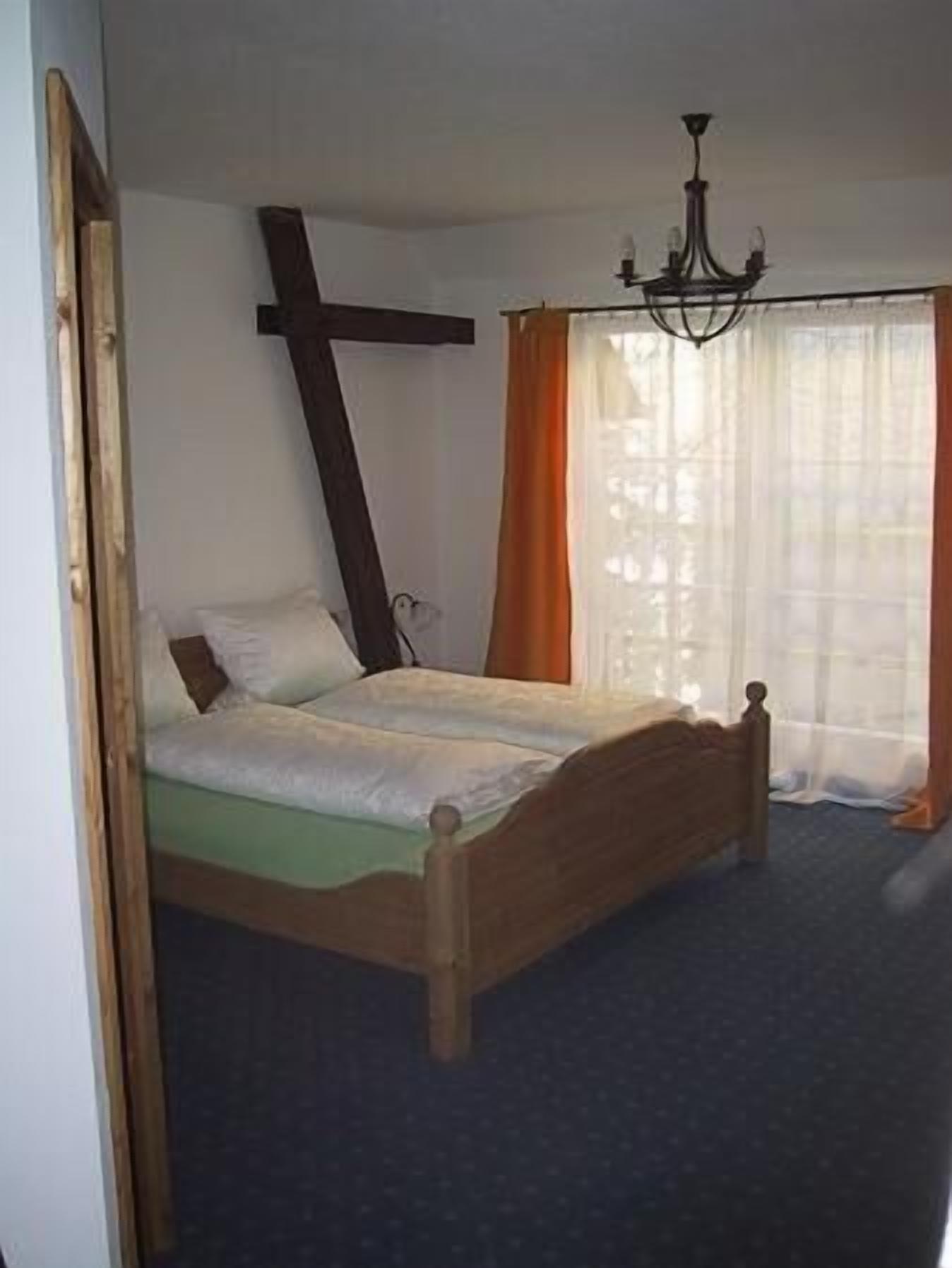 A bedroom with a wooden bed, a cross on the wall, and a chandelier.