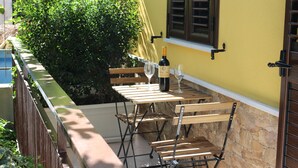 Un balcón con una mesa dispuesta para dos personas, una botella de vino y una ventana con contraventanas.