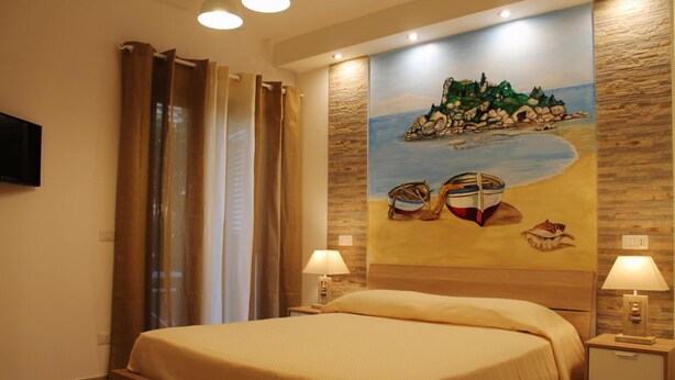 Habitación de hotel con una cama, dos mesitas de noche con lámparas, un cuadro de una playa en la pared y una cortina en la ventana.