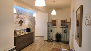 Zona de recepción con mostrador de madera, una obra de arte en la pared y una vitrina de cristal con botellas de vino.
