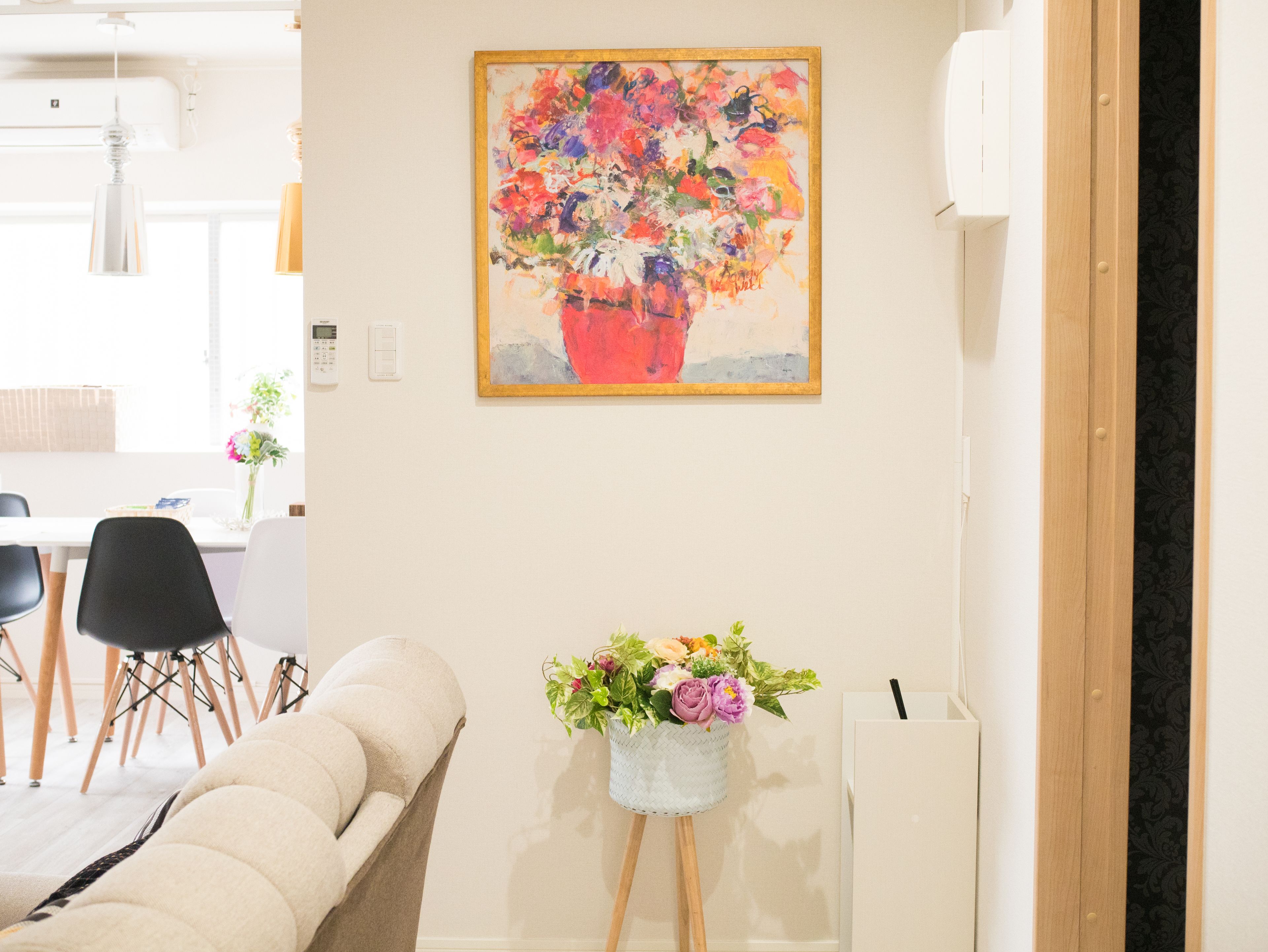 A room with a beige sofa, a small table with a vase of flowers, and a painting of a floral arrangement on the wall.
