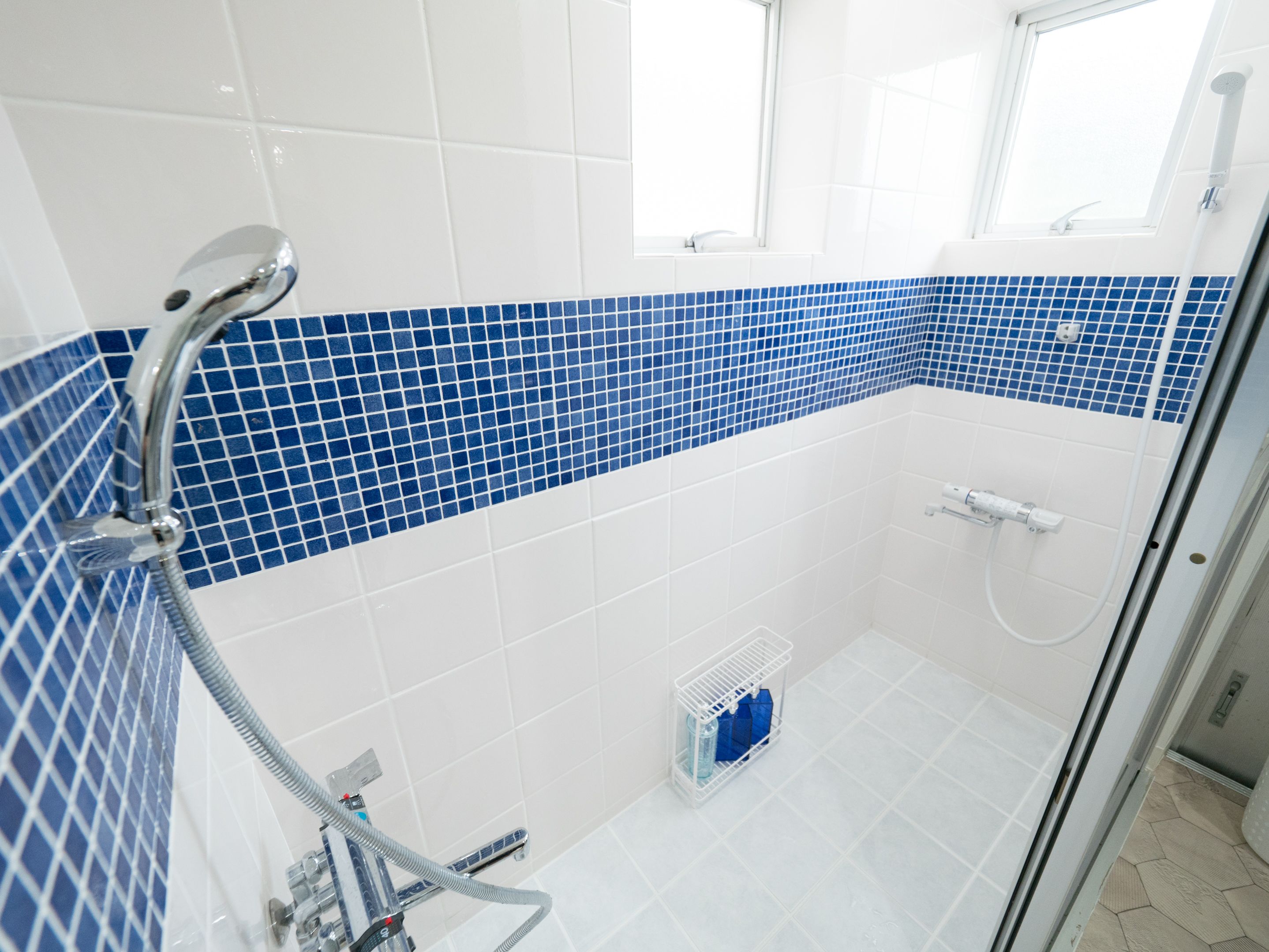 Ein modernes Badezimmer mit Dusche, Wänden in weißen und blauen Fliesen, einer Glasduschtür und einem kleinen Fenster.
