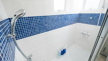 Ein modernes Badezimmer mit Dusche, Wänden in weißen und blauen Fliesen, einer Glasduschtür und einem kleinen Fenster.
