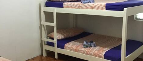 A bunk bed room with a patterned bedspread, a ladder, and a box of tissues.