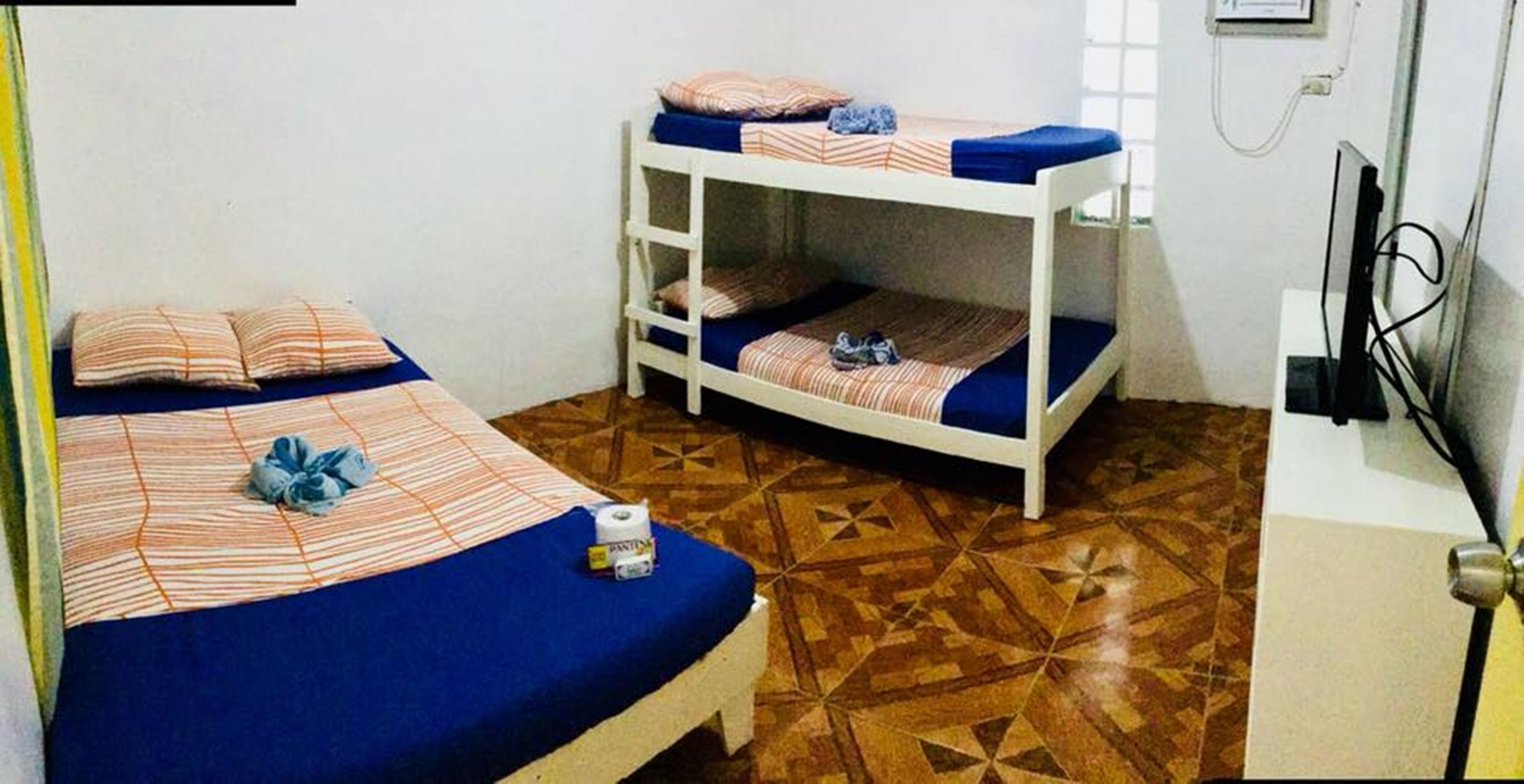 A room with two bunk beds, a small table with a chair, a television, and a patterned floor.