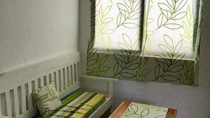 A small room with a white bench, a wooden table, and a window with leaf-patterned curtains. - Rob and Fred's Resort (Boracay Island)