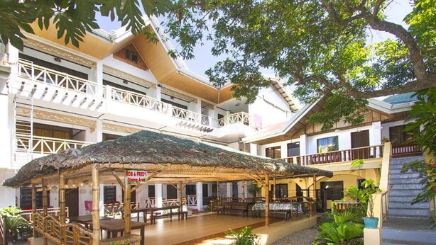 A dining area with a thatched roof, surrounded by a multi-story building with balconies and a pool. - Rob and Fred's Resort (Boracay Island)