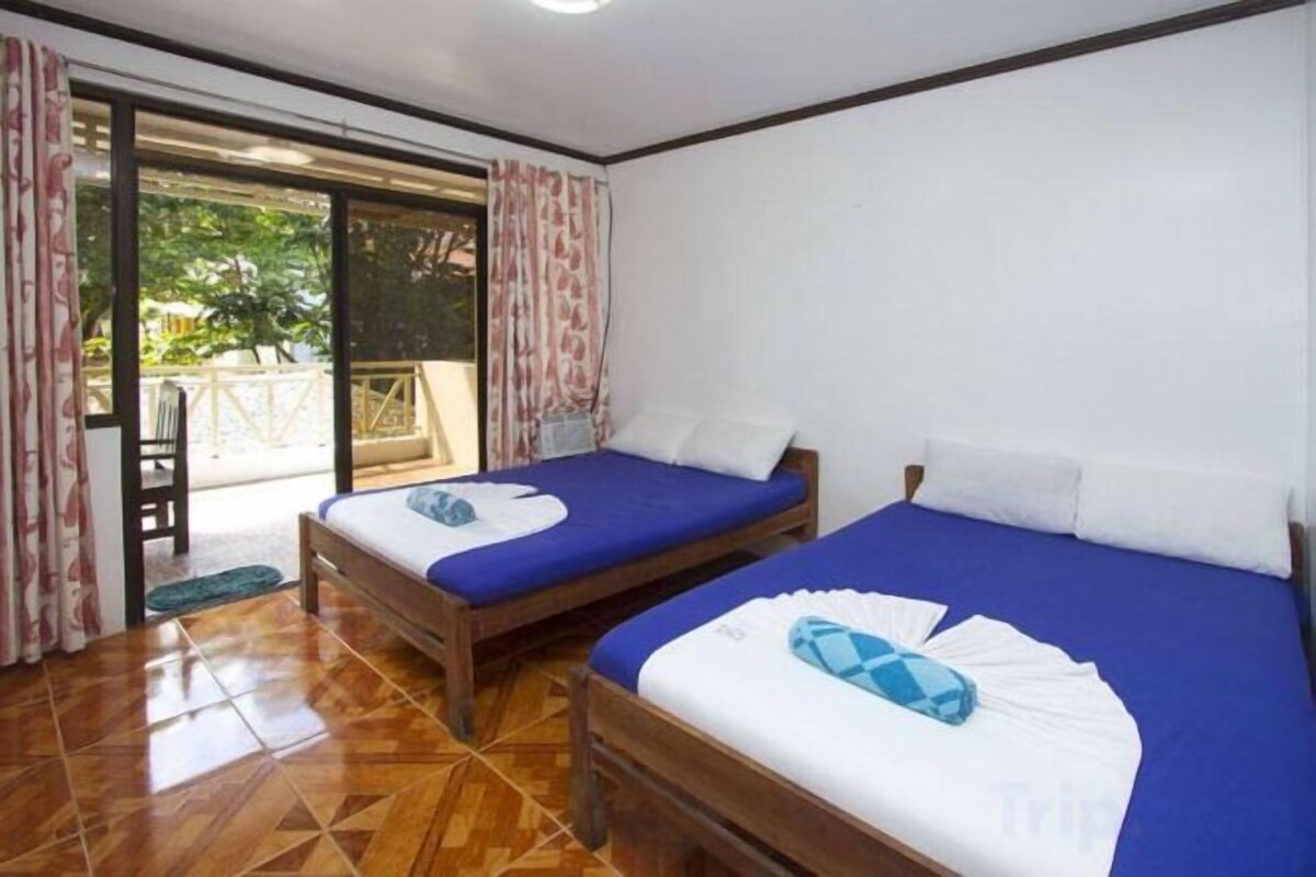 Habitación con dos camas, una puerta corrediza de vidrio que da a un espacio exterior y suelo de madera.