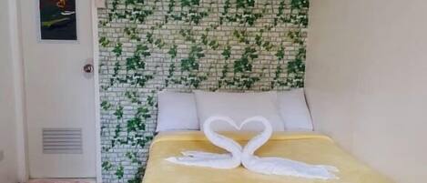 A room with a bed, a door, a wall with a brick pattern, and a tiled floor.