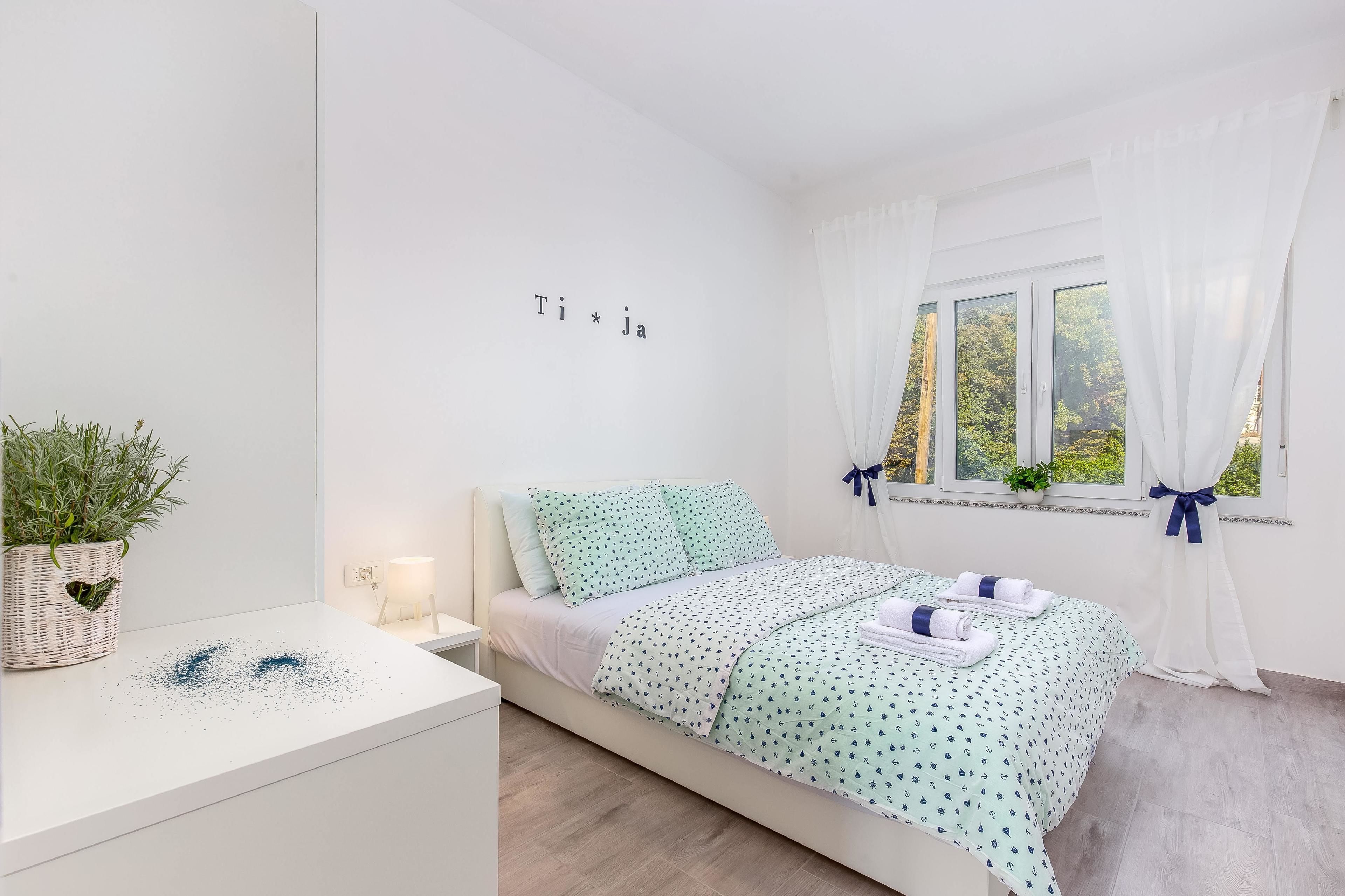 Ein ordentlich eingerichtetes Schlafzimmer mit einem Bett, einem Nachttisch, einer Topfpflanze und einem Fenster mit Vorhängen.