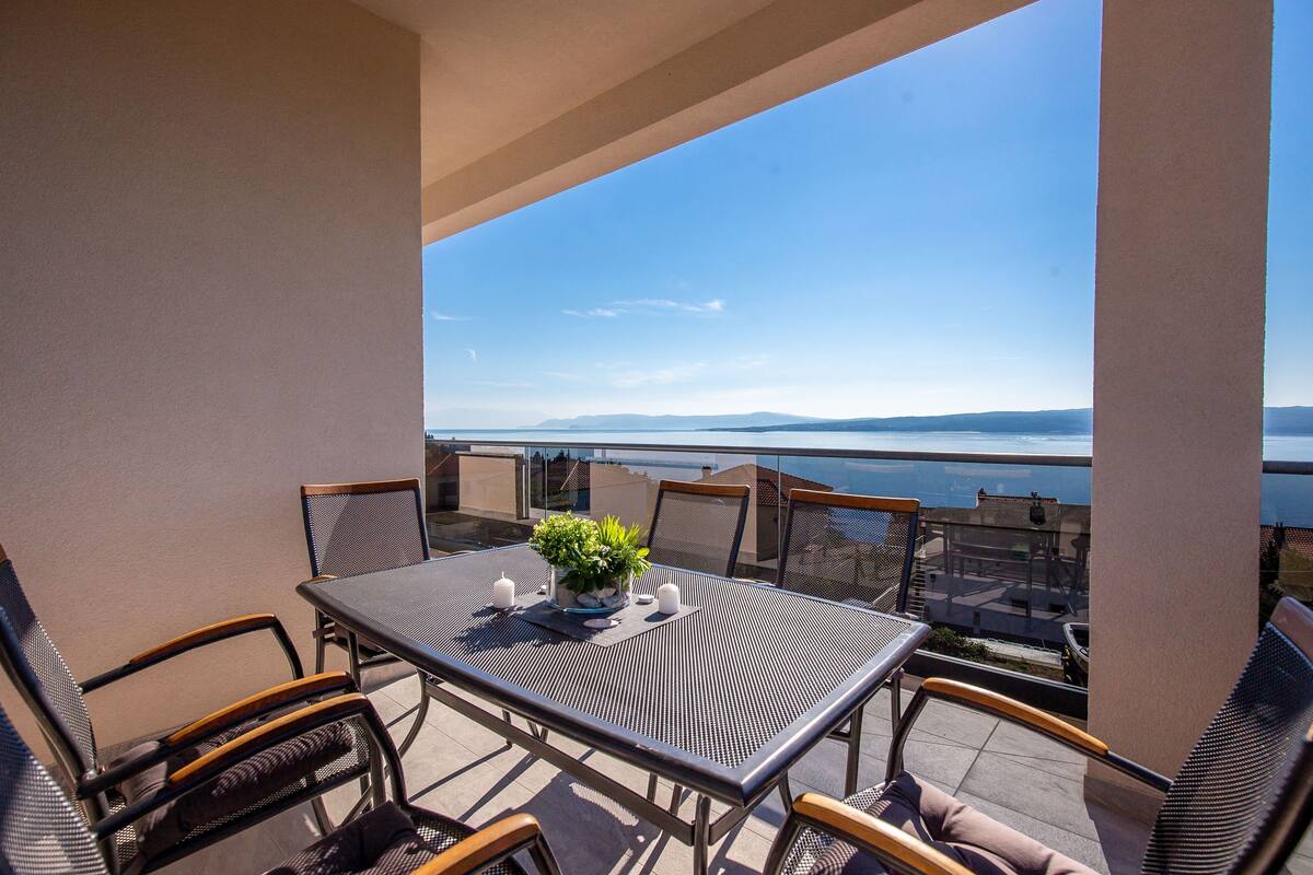 Ein Balkon mit Tisch und Stühlen mit Blick auf ein Gewässer und entferntes Land.