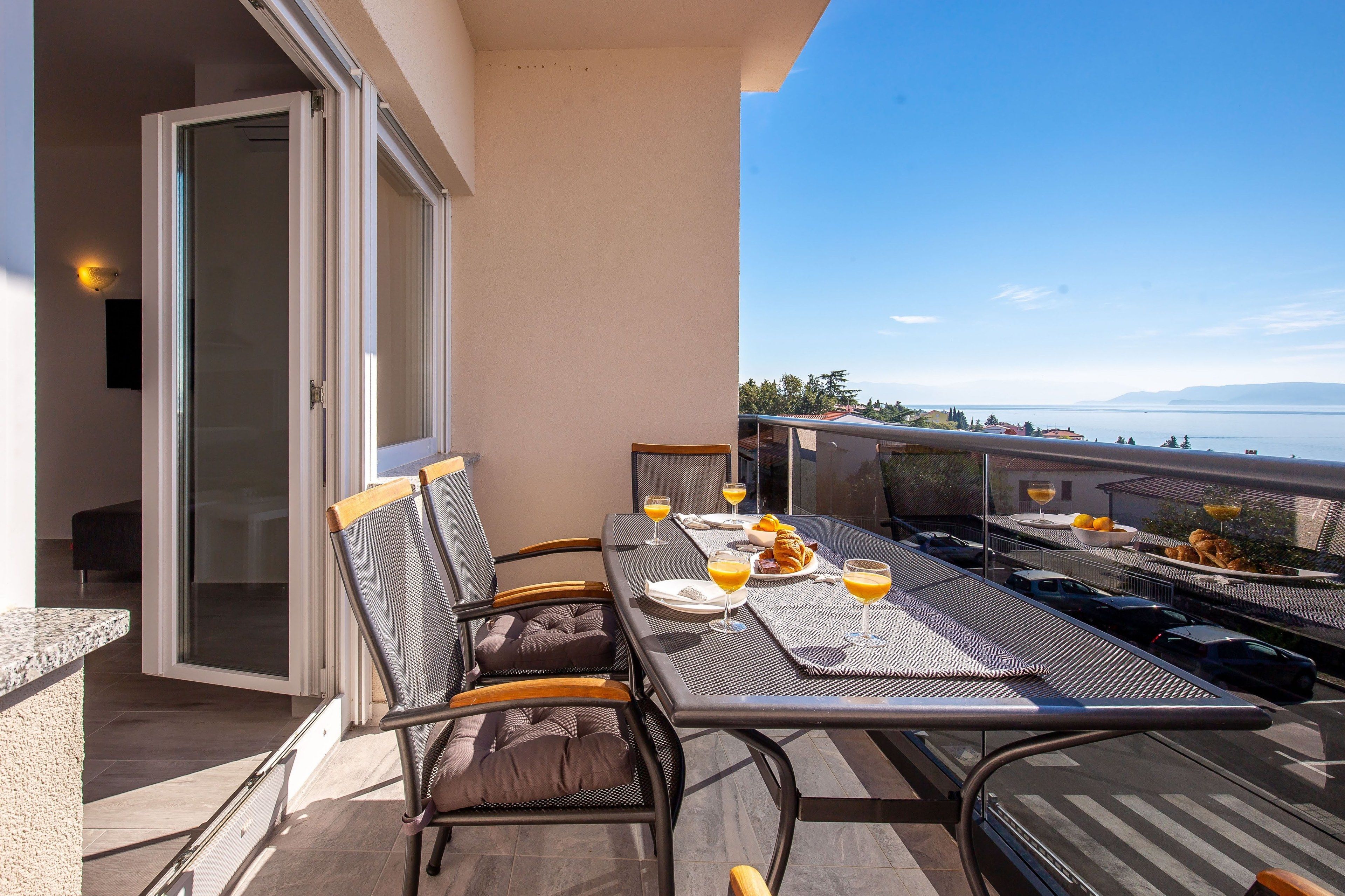 A balcony with a table set for breakfast, including croissants, orange juice, and a plate of food.