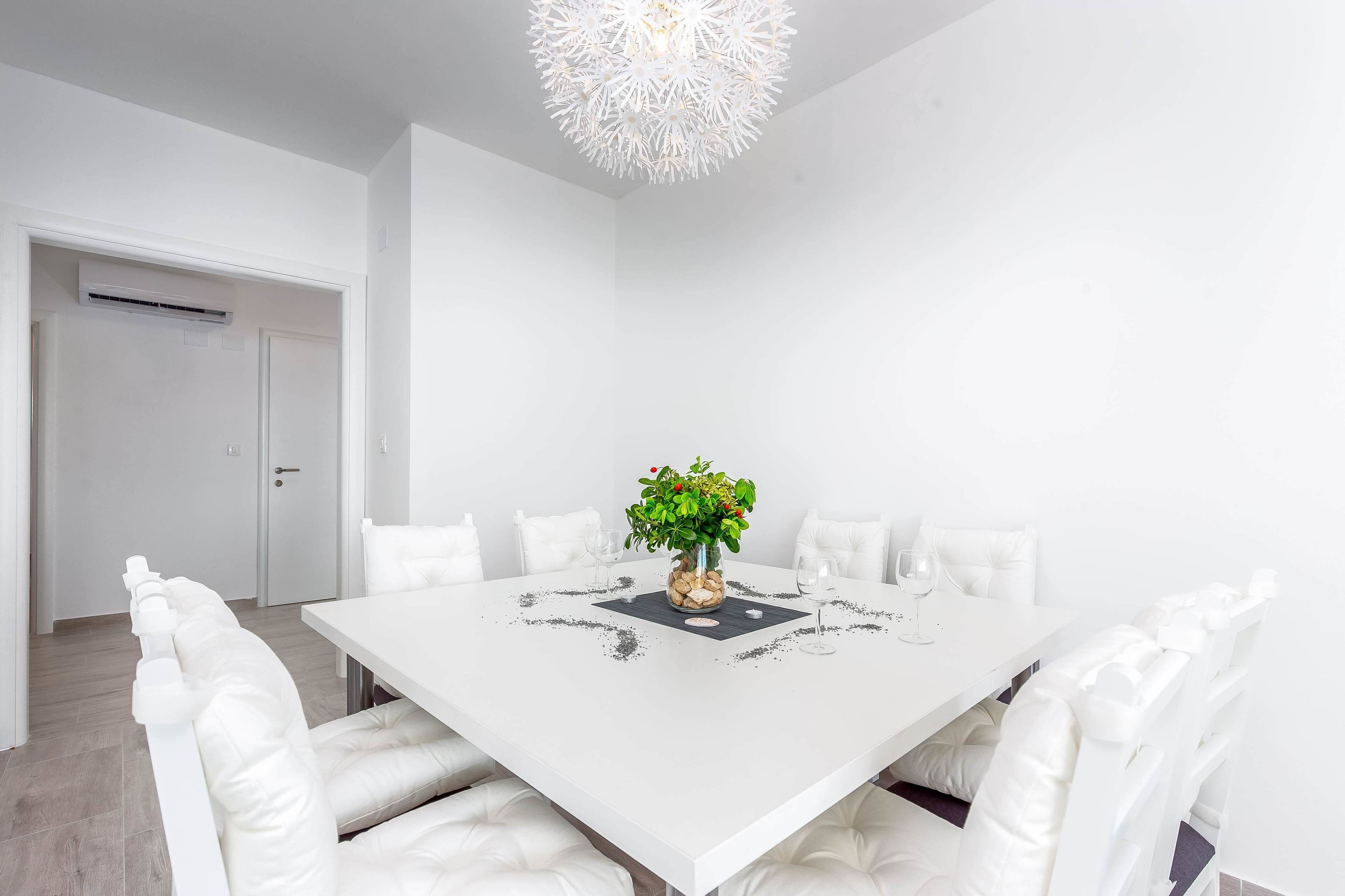 A white dining room with a central table, white chairs, and a decorative plant centerpiece.