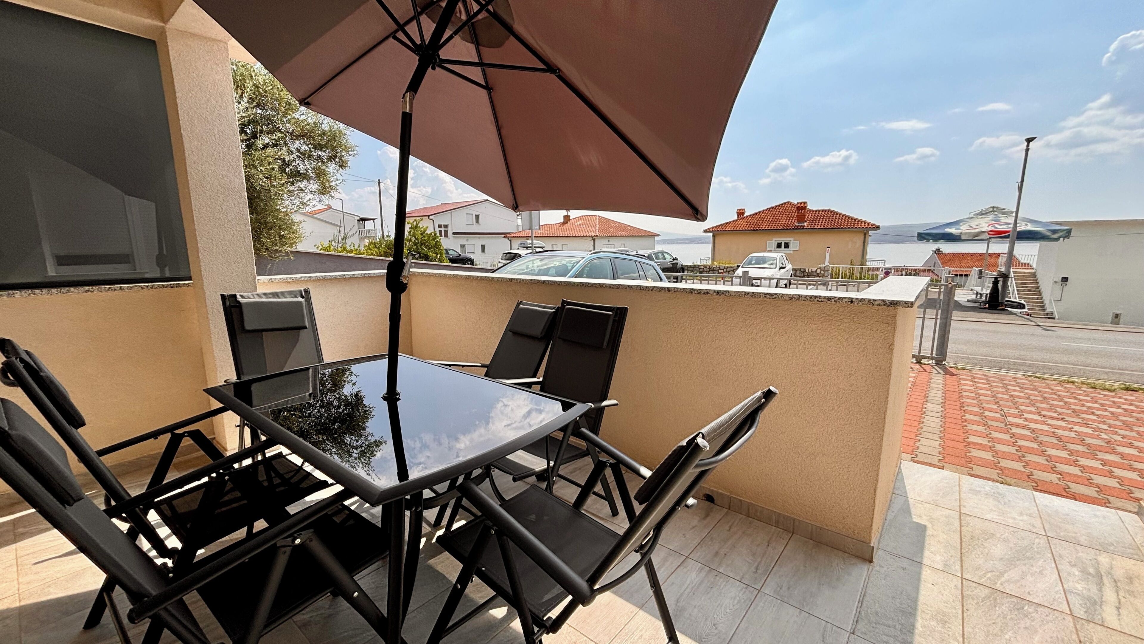A balcony with a table and chairs, a large umbrella, and a view of the street and buildings.