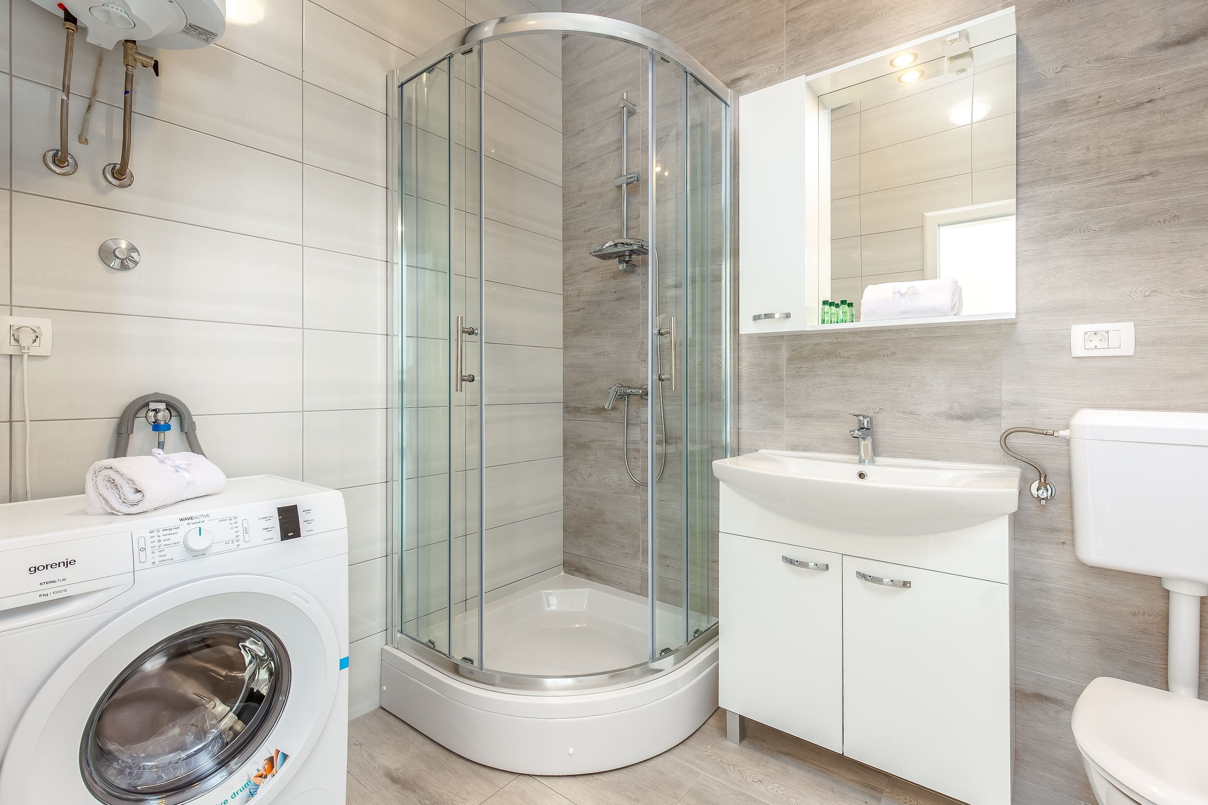 A modern bathroom with a glass-enclosed shower, a washing machine, and a sink.