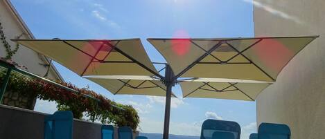 A sunlit outdoor seating area with umbrellas and lounge chairs, overlooking a body of water.
