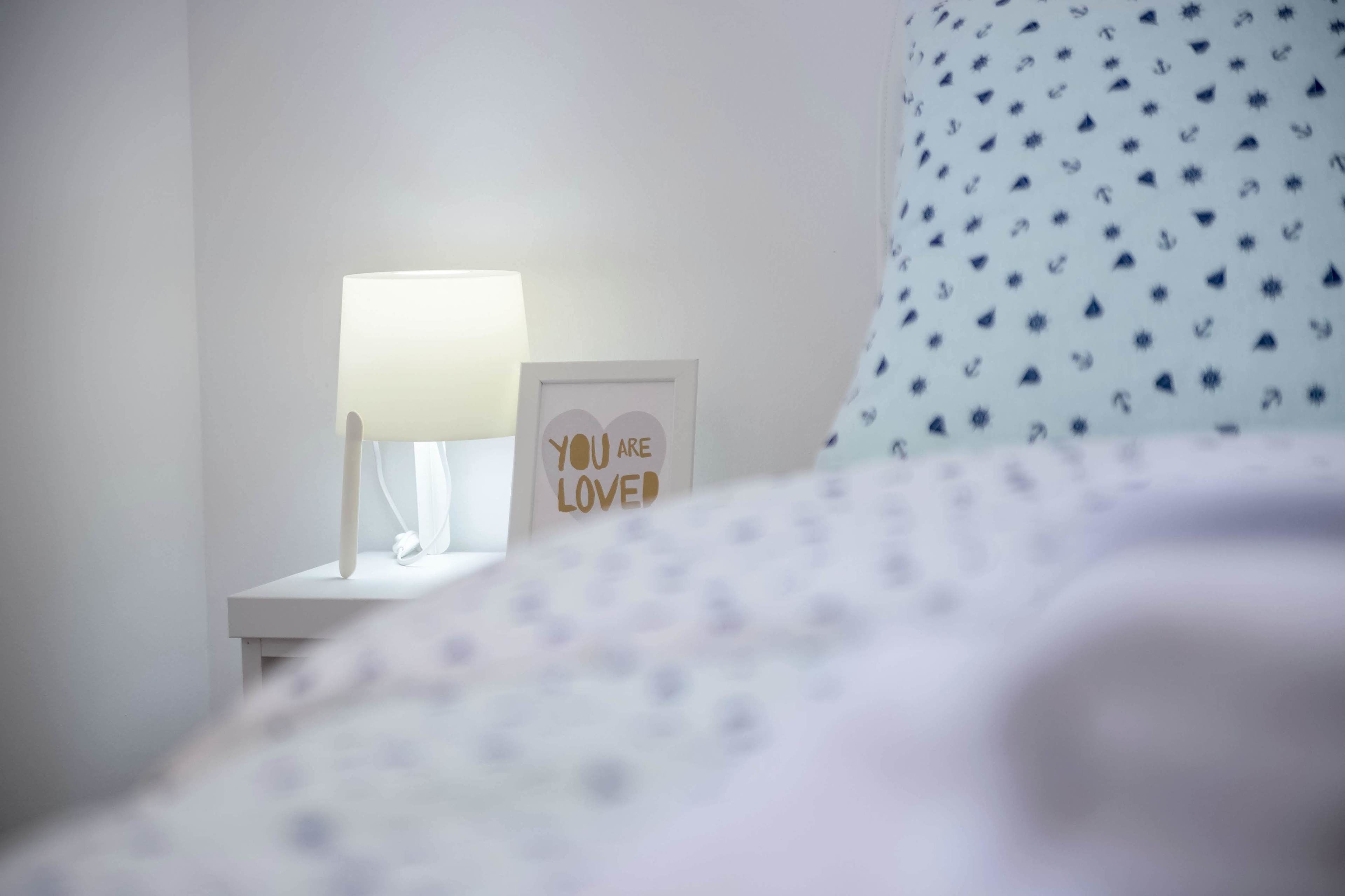 A neatly made bed with a white and blue patterned pillow, a bedside lamp, and a framed inspirational quote on a white nightstand.