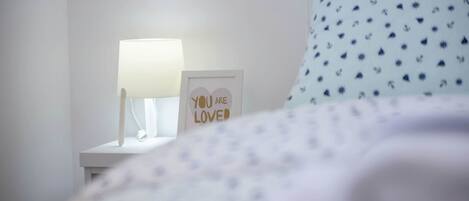A neatly made bed with a white and blue patterned pillow, a bedside lamp, and a framed inspirational quote on a white nightstand.