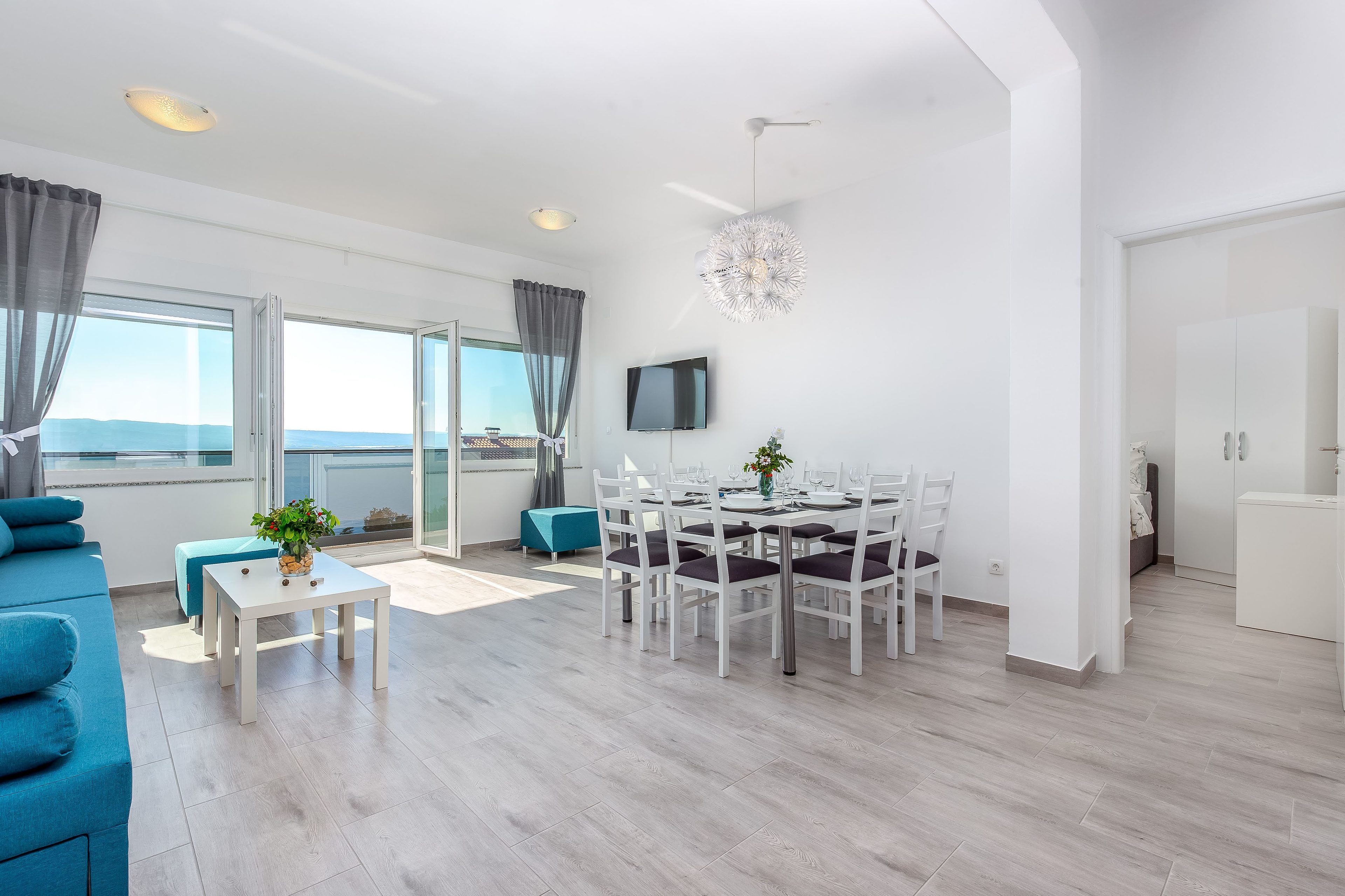A modern living room with a dining area, large windows, and a flat-screen TV.