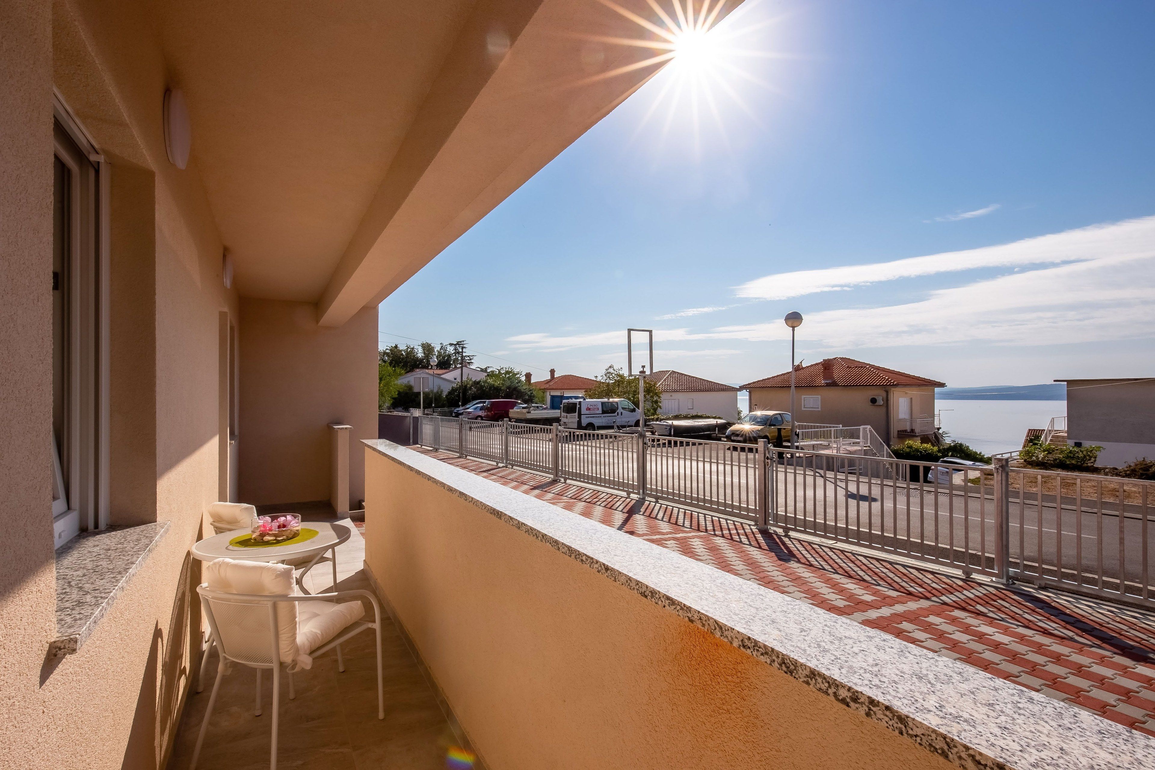A balcony with a table and chairs, a view of the street, and a clear sky.