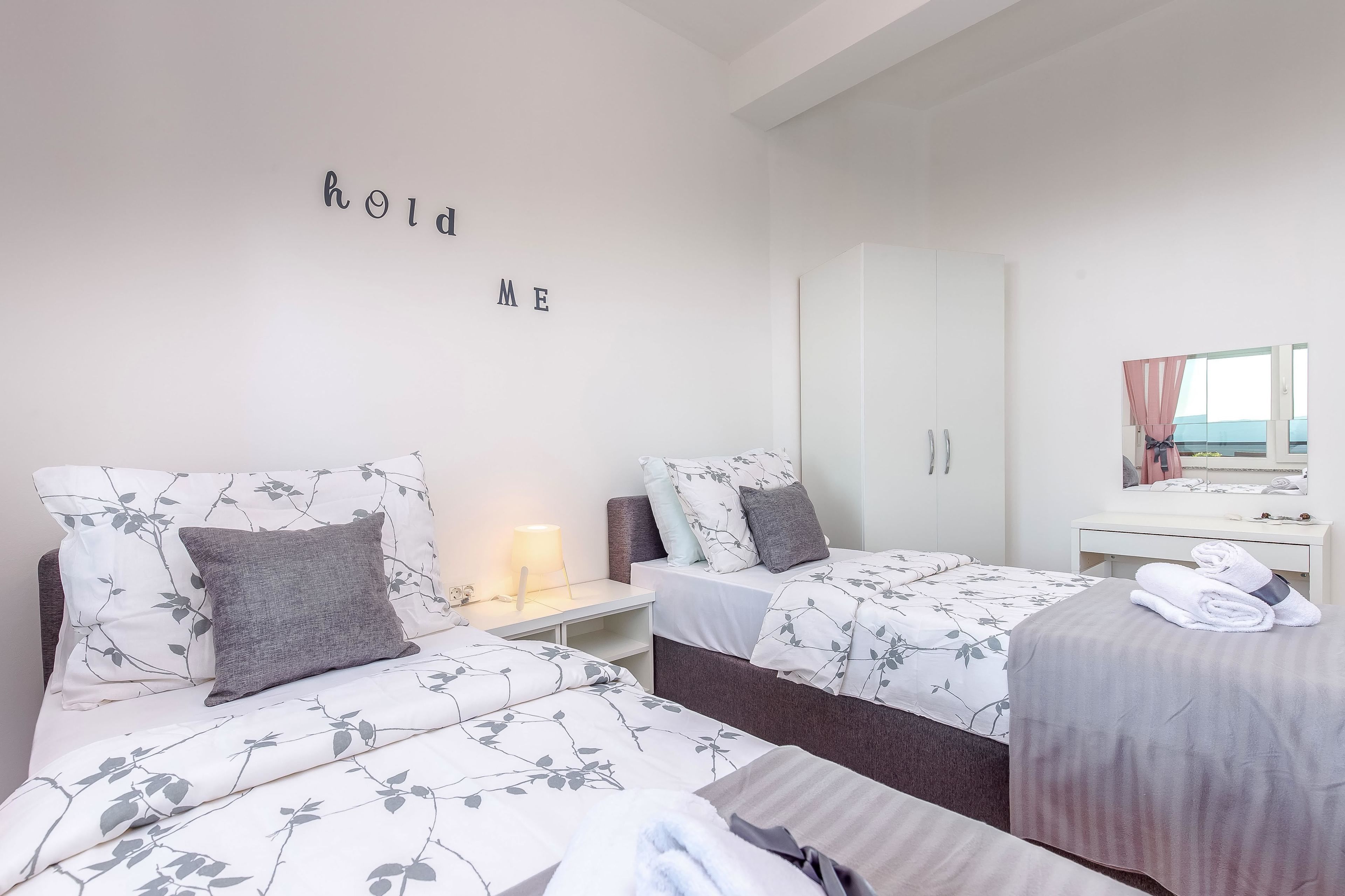A hotel room with two beds, a wardrobe, a desk with a lamp, and a mirror.