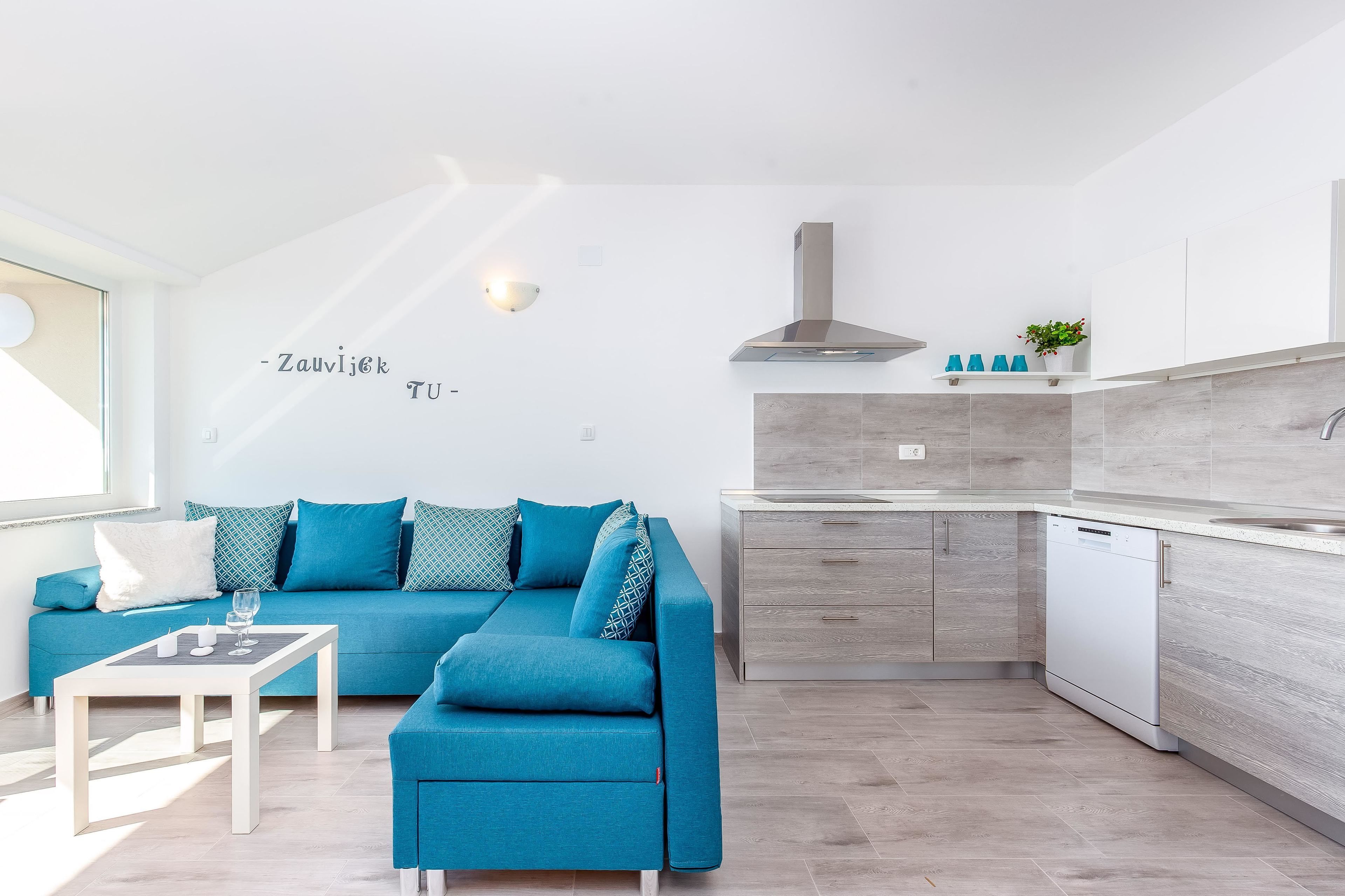 A modern living room with a blue sofa, a coffee table, and a kitchen area with a dishwasher.