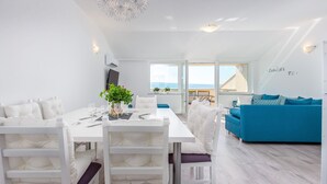 A modern living space with a dining area, a blue sofa, and a view of the sea.