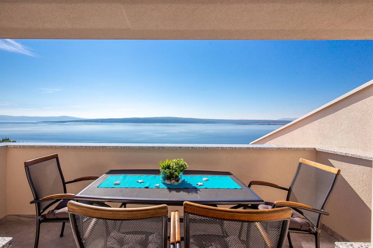 Ein Balkon mit Tisch und Stühlen, Blick auf das Meer und einer Pflanzendekoration.