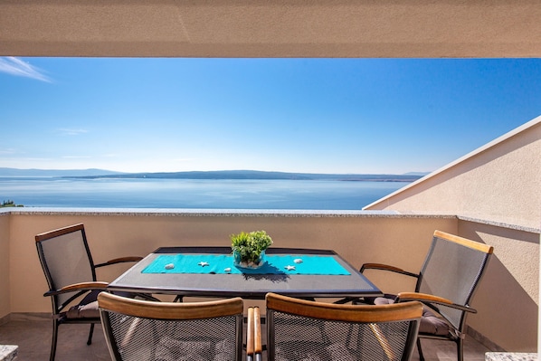 A balcony with a table and chairs, a potted plant, and a view of the sea. - Villa Veronique (Crikvenica)