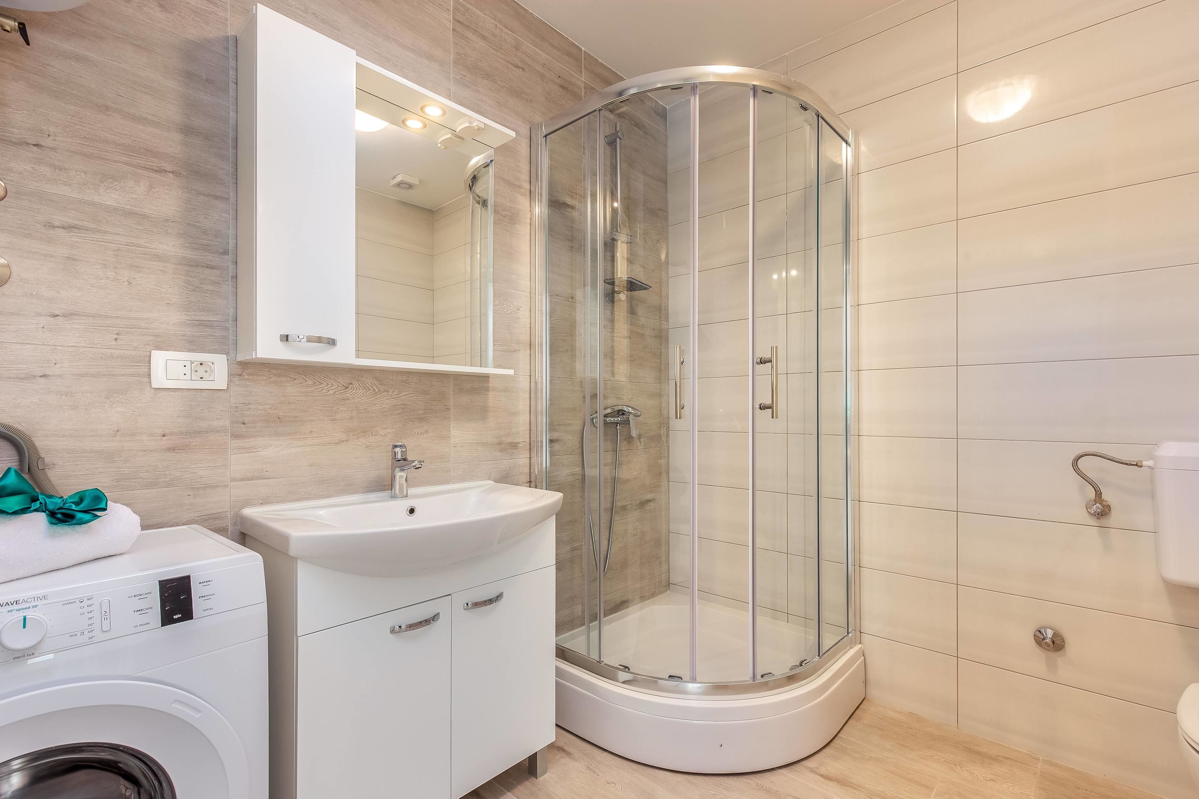 Un bagno moderno con doccia vetrata, lavandino e lavatrice.