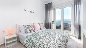 A bedroom with a bed, a nightstand with a lamp, a wall with the text "Dreams...", and a view through a large window.