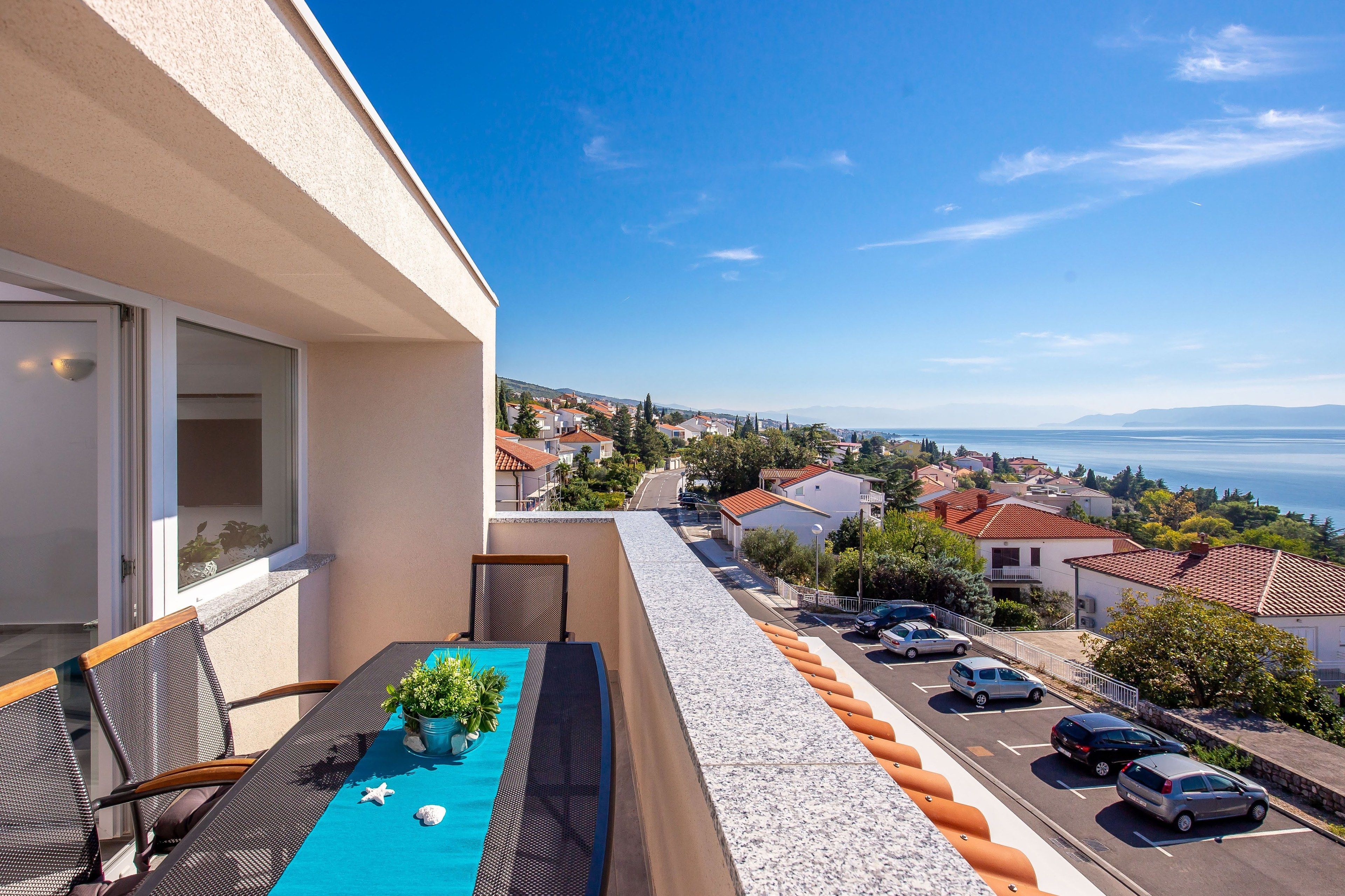 A balcony with a table, chairs, and a view of a coastal town.