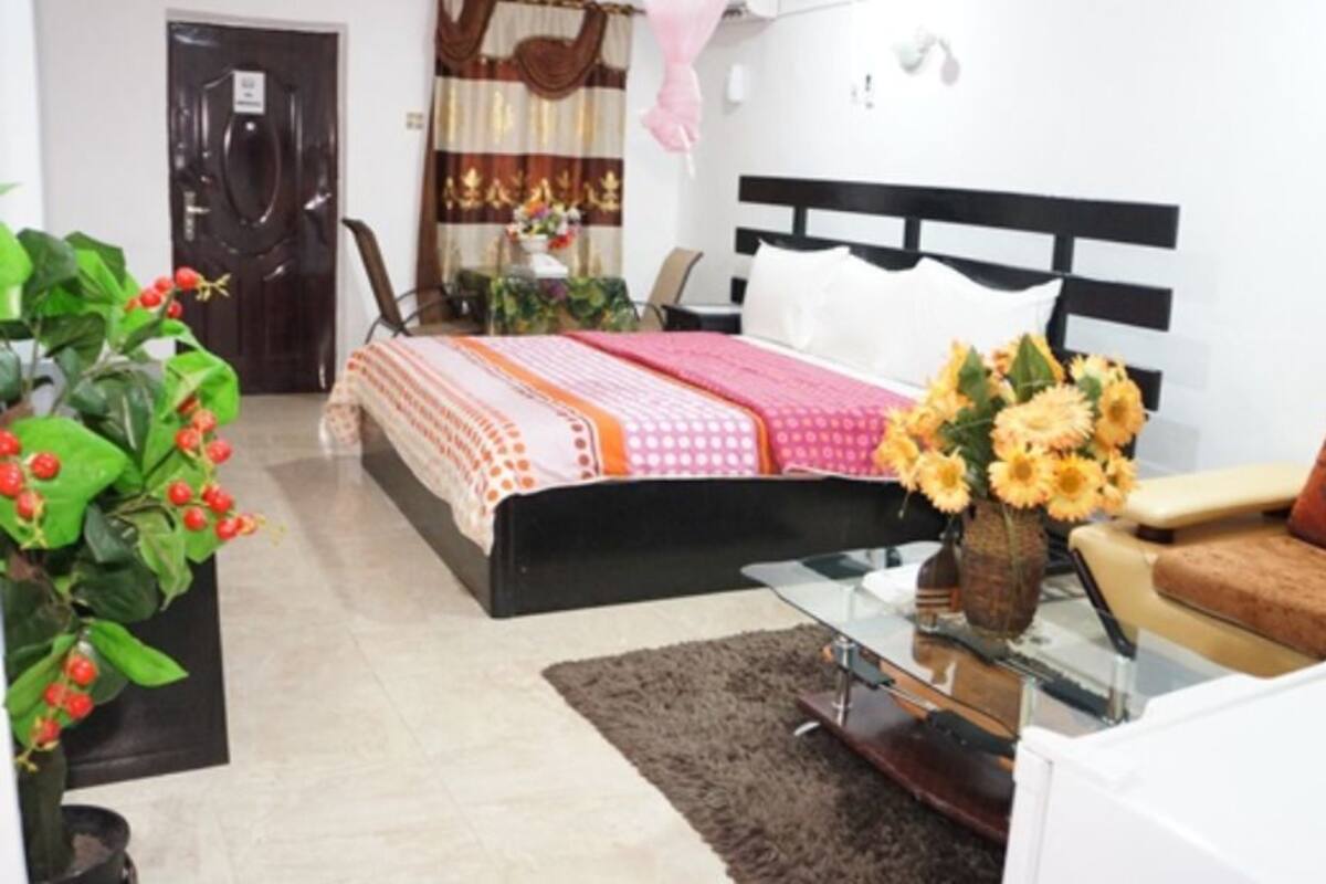 A hotel room with a bed, a sofa, a glass coffee table, and a potted plant.