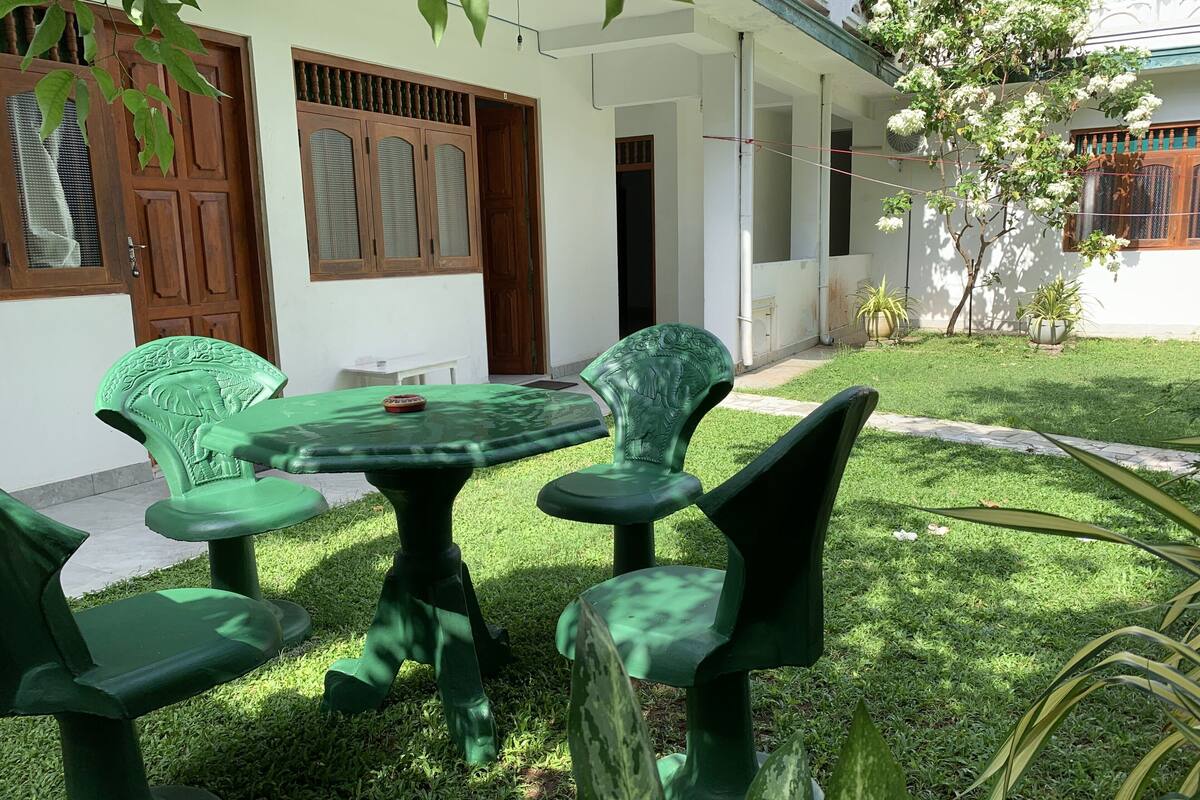 A green plastic table and chairs set on a lawn in front of a building with a white exterior and wooden doors.