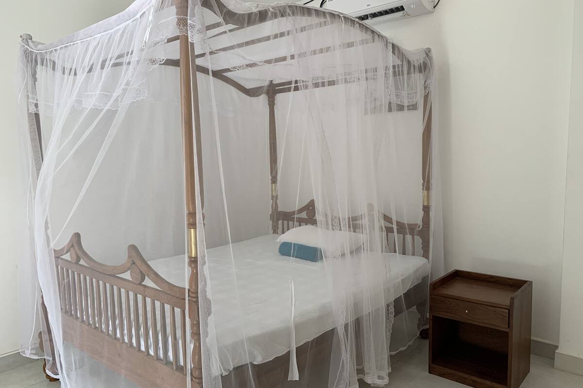 A four-poster canopy bed with a wooden frame and white bedding.