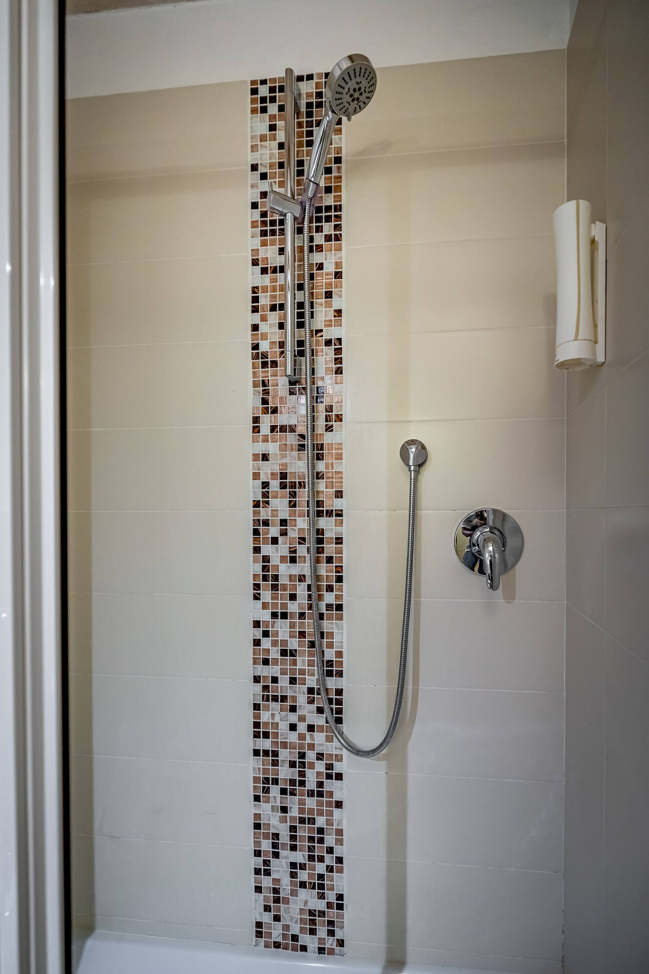 A shower with a vertical tile design, a handheld showerhead, and a wall-mounted faucet.