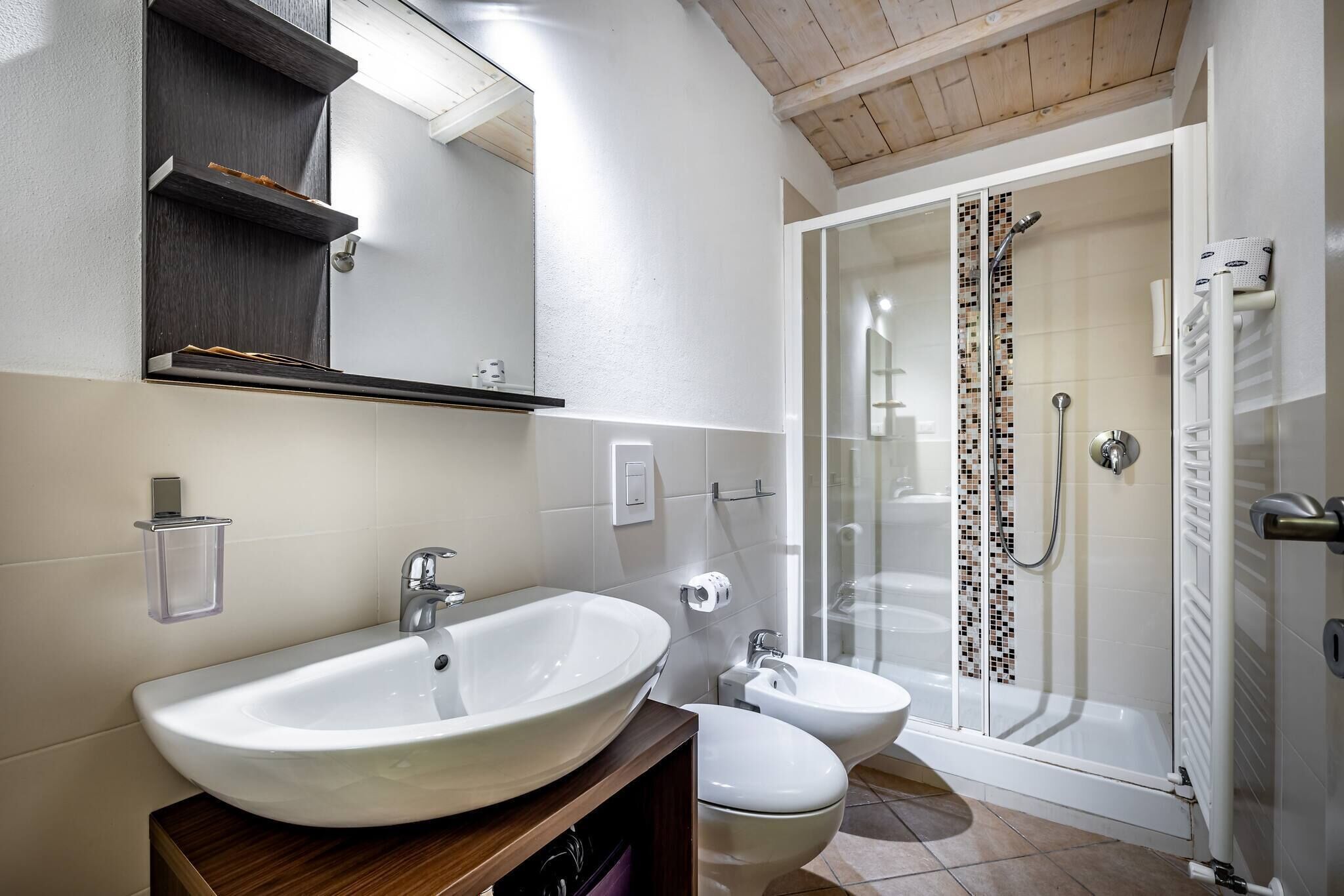 Un bagno moderno con un lavandino ampio, due servizi igienici, cabina doccia e soffitto in legno.