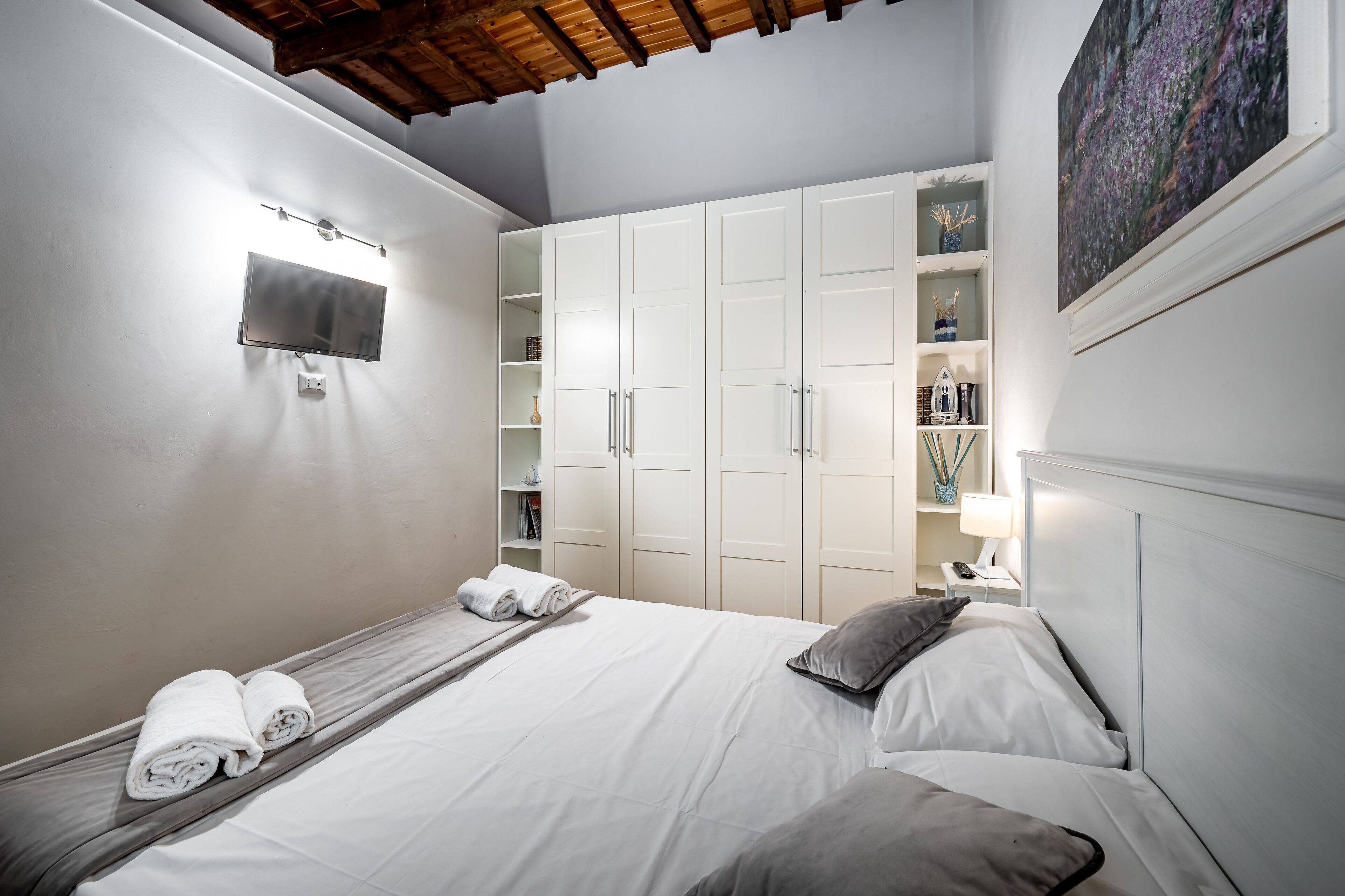 A bedroom with a bed, a TV mounted on the wall, and a wardrobe with shelves.