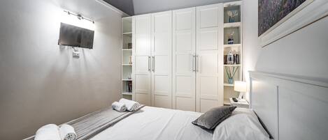 A bedroom with a bed, a TV mounted on the wall, and a wardrobe with shelves.
