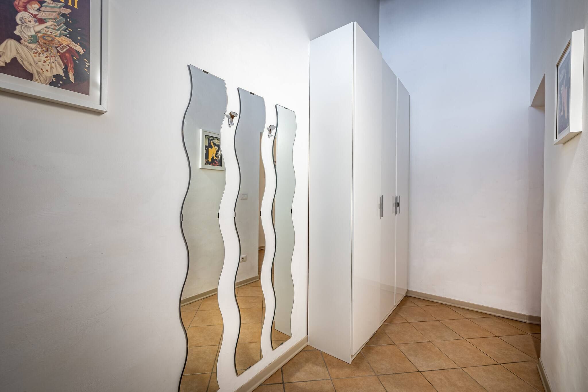 A hallway with a white wardrobe, a wavy mirror, and a framed picture on the wall.