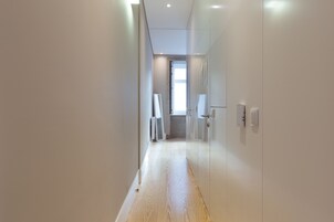 A hallway with wooden flooring, white walls, and a door leading to a room.