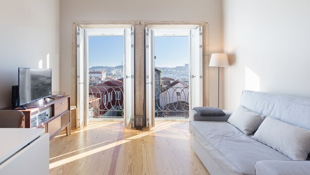 A modern living room with a sofa, TV, and a view through open doors to a balcony with a cityscape. - Porto and Clérigos Views by Porto City hosts (Porto)
